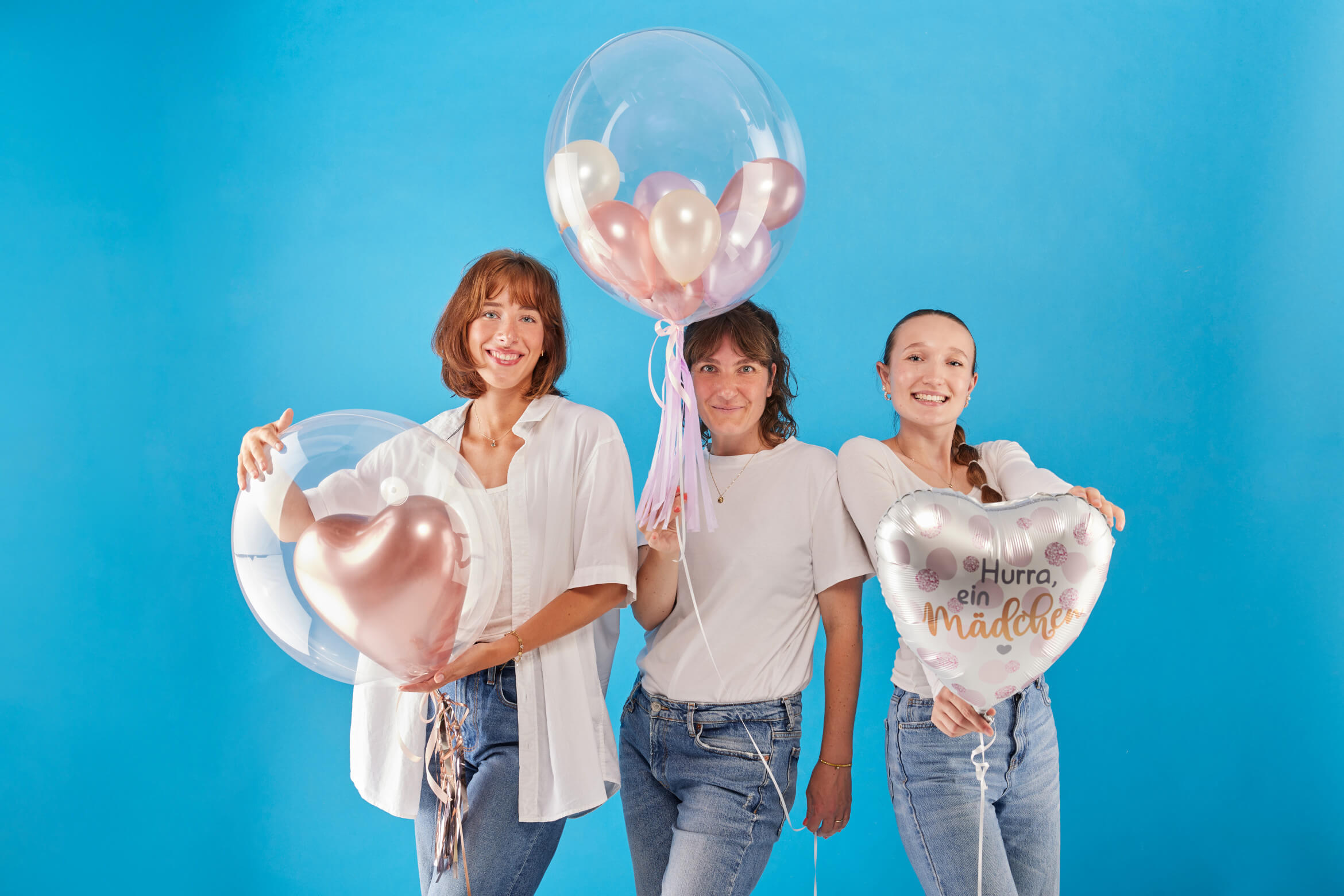 Drei Frauen halten Ballons vor einem blauen Hintergrund